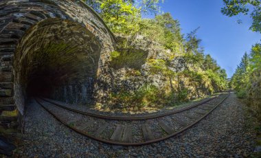 Thüringen Almanya 'sında mavi gökyüzünün altından geçen yeşil ormandaki tek raylı taş demiryolu tünelinin panoramik manzarası