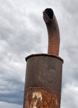 Old rusty exhaust pipe with muffler against the sky.