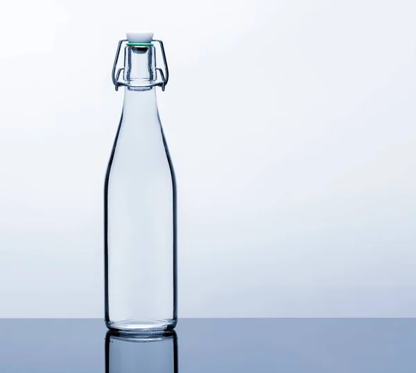 Water bottle closed with a ceramic stopper. A bottle placed on a black glass table, the background evenly blue.