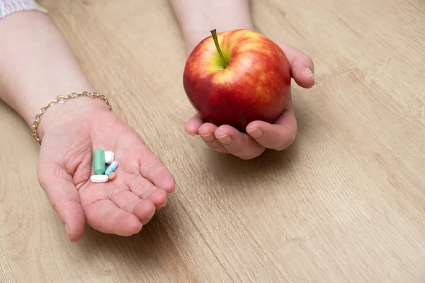 A woman holding pills in one hand and an apple in the other.