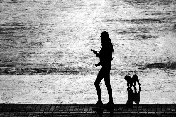 The outline of a girl and a dog against the sunlit concrete background.