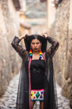 Genç And kızı Cusco Peru 'da Ollantaytambo' da poz veriyor. Peru 'dan halk kıyafetleri giyen genç bir latin manken. Cusco 'daki İnka döneminden geleneksel mimari.