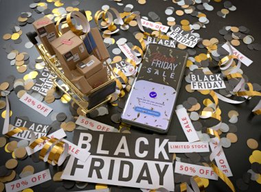 Akıllı telefonlu Kara Cuma konsepti, kutu dolu alışveriş arabası ve şenlikli konfeti. Çevrimiçi alışveriş, e-ticaret indirimleri ve bayram perakende satış promosyonu..