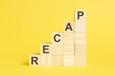 RECAP kelimesi tahta küp piramidin üzerine yazılır. Parlak sarı arkaplan üzerindeki bloklar