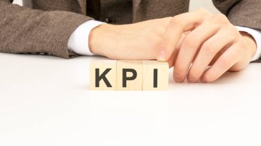 Genç adamın elini beyaz gömlekli, tahta bloklu, beyaz masadaki Kpi yazıları için kapat..