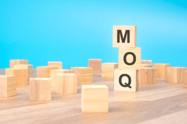 MOQ - asgari düzenin kısaltması - tahta küp üzerine yazılmış, iş konsepti. mavi arkaplan