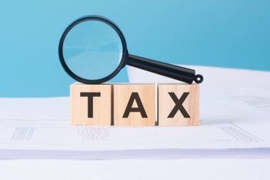 Mavi arkaplandaki ahşap küplerle ilgili vergi sözcüğü büyüteç ve iş belgeleriyle.