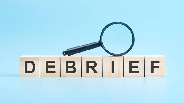 stock image wooden blocks with a magnifying glass text: DEBRIEF. blue background