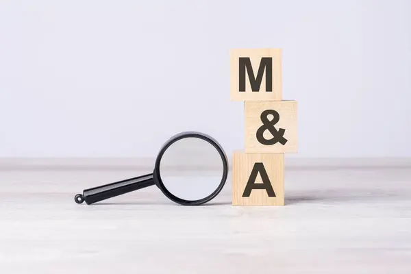 M and A - or Mergers and Acquisitions concept. text on wooden cubes under a magnifying glass.