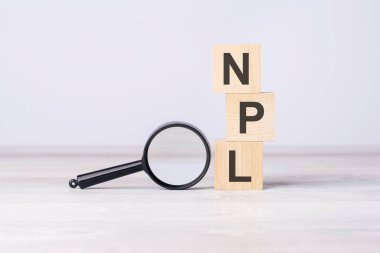 NPL - or Non Performing Loans concept. text on wooden cubes under a magnifying glass. clipart