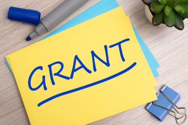 Grant - Kırtasiyeyle birlikte açık ahşap zemin üzerinde sarı kağıt üzerinde metin.