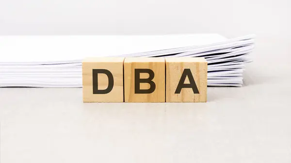 text DBA - Data Base Administrator made with wood building blocks, stack white paper on background
