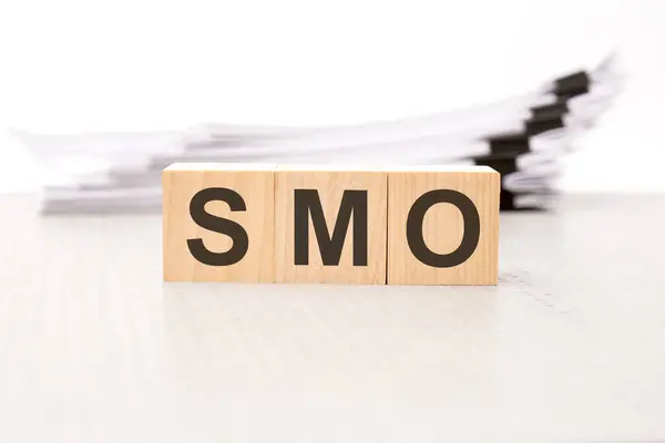 text smo - social media optimization - on wooden blocks. the background is a business papers. finance concept. white background