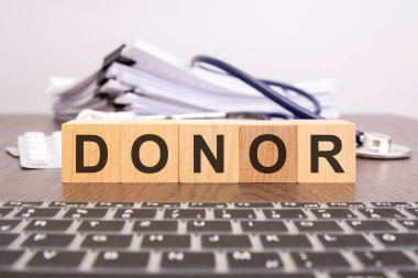 Tahta küpler steteskop, hap, doktorun masaüstündeki not defteri ve tıbbi konsept ile DONOR harflerini oluşturur.