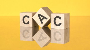 Sarı arka planda CAC kısaltmalı üç tahta küp. Cam yüzey kavramındaki bir görüntünün yansıması