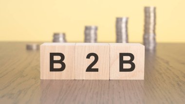B2B Business To Business kısaltması ahşap bloklar ve sarı arka planda paralar üzerine yazılmış