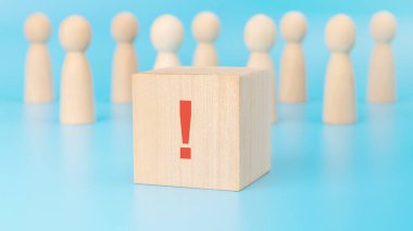 Mavi bir yüzey üzerinde ünlem işareti olan ahşap bir küpün yakın çekimi, arka planda tahta çubuk figürler.