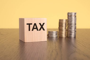 Tahta küplerin ön görüntüsü, üzerinde sarı arka planda bozuk paralar olan TAX yazılı. Vergi ödeme ve mali planlama sürecini sembolize ediyor