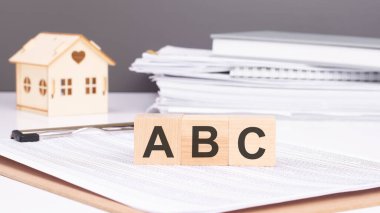 Tablolu bir belgede ABC yazılı tahta küpler. Arkaplan: Ahşap bir ev figürü ve belge yığını. Konsept: Gayrimenkul 'de Eğitim Vakıfları.