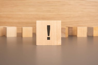 Yakın plan: üzerinde ünlem işareti olan tahta bir küp masanın üzerinde duruyor, arka planda küçük tahta bloklar. Mesajın aciliyeti ve önemini sembolize ediyor.