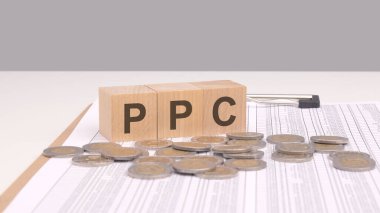 Tahta bir masanın üzerindeki tahta bloklara altın sikkelerle PPC 'yi mesaj at. PPC, reklamcıların reklamları her tıklandığında bir ücret ödedikleri dijital pazarlama modeli olan Pay-Per-Click 'i temsil ediyor..