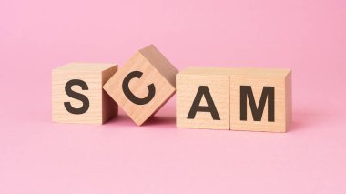 Pembe bir yüzeyde SCAM 'i gösteren tahta bloklar hile ya da sahtekarlık olduğunu gösteriyor..