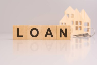 Masanın üzerindeki tahta küplerde mesaj, model ev ve arka planda anahtarlar var. konsept: genellikle gayrimenkul yatırımı veya mülk edinimi için finansal yardım alma kavramı