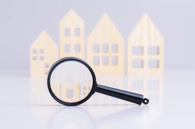 Gri masadaki ahşap evlerin arka planında büyüteç var. Emlakçılık hizmetleri, yeni bir konsept bulmak