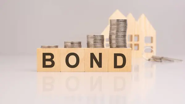close-up of coins on wooden blocks with the word bond in focus. wooden house models are blurred in the background. business in the real estate sector.