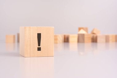 Tahta bir bloğa, aciliyet ve vurguyu vurgulayan ünlem işaretinin yakın plan çekimi. arkaplanda, kişiselleştirme potansiyelini sembolize eden gri bir arkaplan üzerinde boş tahta küpler yer almaktadır