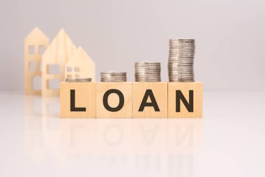 Borç sözcüğünün odak noktasında olduğu tahta bloklardaki bozuk paraların yakın çekimi. Ahşap ev modelleri arka planda bulanıklaşıyor. konsept: kredilerle emlak finansmanı