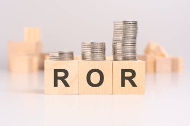 wooden blocks with the word ROR and stacked coins on a light background, in the background a blurred image of many wooden cubes haphazardly arranged clipart