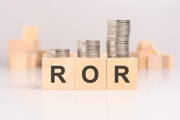 wooden blocks with the word ROR and stacked coins on a light background, in the background a blurred image of many wooden cubes haphazardly arranged