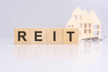 RİT 'i kodlayan ahşap küplerin yanında bir model ev ve arka planda anahtarlar, kira işlemi veya mülk yönetimi bağlamını gösteriyor. Gayrimenkul Yatırım Vakfı kavramı