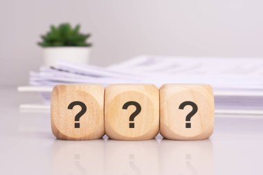 Ofis masasında üç soruyu heceleyen ahşap küpler, arka planda beyaz kağıt bir belge, finansal planlama, uyum ile ilgili bir iş konsepti iletir