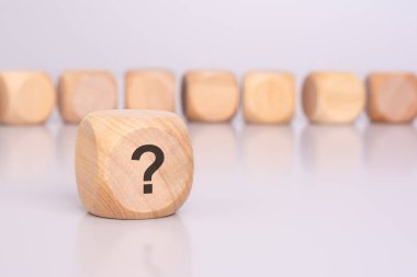 Ön planda, üzerinde soru işareti ve masa yüzeyinden yansıması olan bir tahta blok var. Arka planda bir sıra tahta bloklar (odak dışı) var).