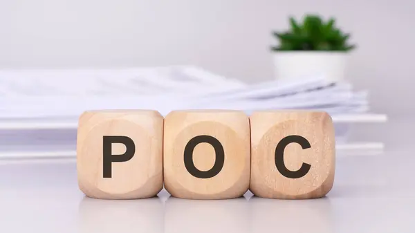 wooden cubes spelling out \'POC\' on the office table, with a white paper document on the background, poc - short for proof of concept