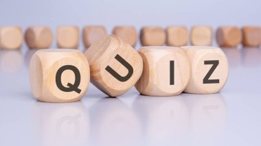 Dört ahşap blok üzerinde QUIZ harfleri olan açık gri bir tablo üzerinde izleyiciye bir açı ve yüzeyin yansıması. Arka planda yazılı olmayan bir sürü küp var.