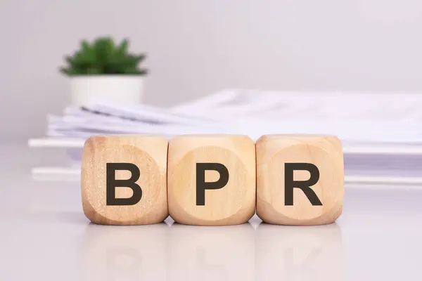 wooden cubes spelling out \'BPR\' on the office table, with a white paper document on the background, bpr - short for business process reengineering
