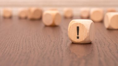 Ön planda ünlem işareti ve masa yüzeyinden yansıması olan bir tahta küp var. Arka planda bir sıra tahta bloklar (odak dışı) var).