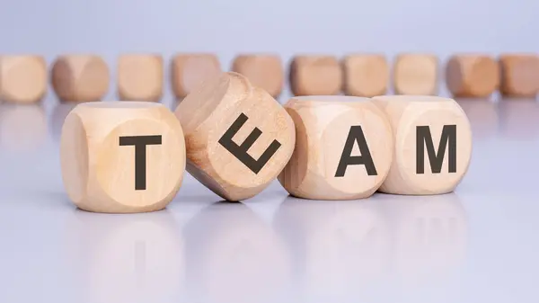 stock image four wooden blocks with the letters TEAM standing at an angle to the viewer on a light gray table and reflecting of the surface. there are many cubes with no inscription in the background