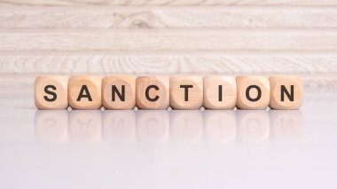 'SANCTION' sözcüğünün yansıması ve ahşap arkaplan ile parlak gri bir yüzey üzerinde sergilendiği ahşap küpleri