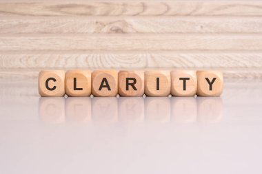wooden cubes displaying the word 'CLARITY' arranged on a glossy gray surface, with a reflection and wooden background