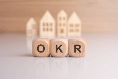 a row of wooden blocks spell out 'OKR - short for Objectives and Key Results' with miniature house models in the background, representing real estate loans clipart