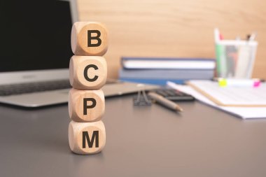 Bir iş belgesi ve not defterinin arka planında 'BCPM' kelimesine seçici bir odaklanma. Kurumsal strateji ve planlamada ticari devamlılığın ve proje yönetiminin önemini ifade eder.