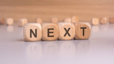 Bu fotoğrafta, yaklaşan adımları, geçişleri, gelecekteki planları veya yaklaşan olayları göstermek için mükemmel olan ahşap zar NEXT yazılıyor. Sunumlarda ve eğitim materyallerinde kullanım için ideal