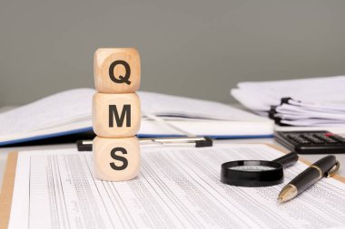 Bloklar Q, M ve S, dokümanlarla dolu bir masanın üzerinde tam bir Kalite Yönetim Sistemi temsil ediyor