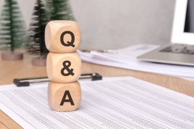 Yaratıcı bir şekilde stilize edilmiş bir soru cevap ekranı sergilenen tahta bloklar evrak işleri ve dizüstü bilgisayarla birlikte bir masanın üzerinde düzenlenmiş.