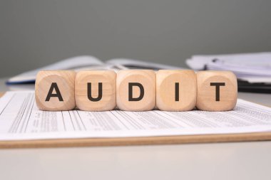 Finansal belgelerin üzerine yerleştirilmiş tahta bloklar ve raporlarla oluşturulan AUDIT kelimesine dikkat edin.