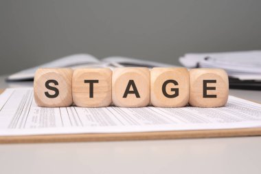 Wooden blocks spelling STAGE placed on a document, symbolizing various stages in life or processes. clipart